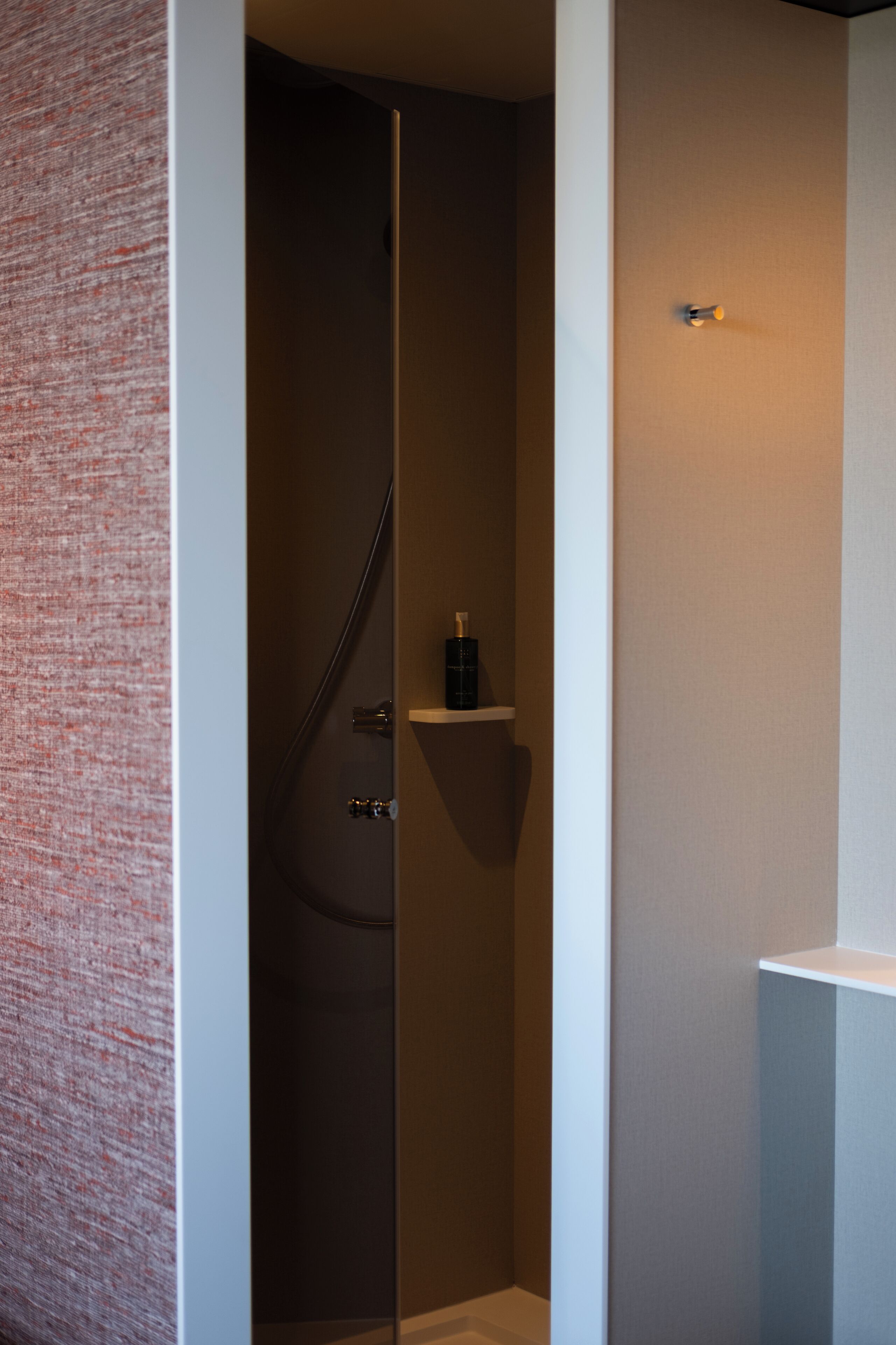 A modern bathroom with a glass shower enclosure, a small shelf with toiletries, and a towel rack.