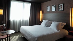 Une chambre d’hôtel avec un grand lit, un bureau avec une chaise, un piano et une fenêtre avec des rideaux.