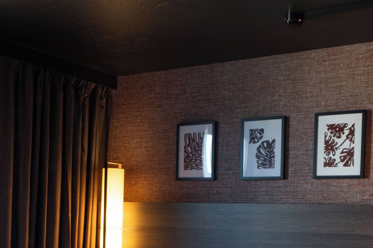 A hotel room with a bed, a nightstand, a lamp, and three framed artworks on the wall.