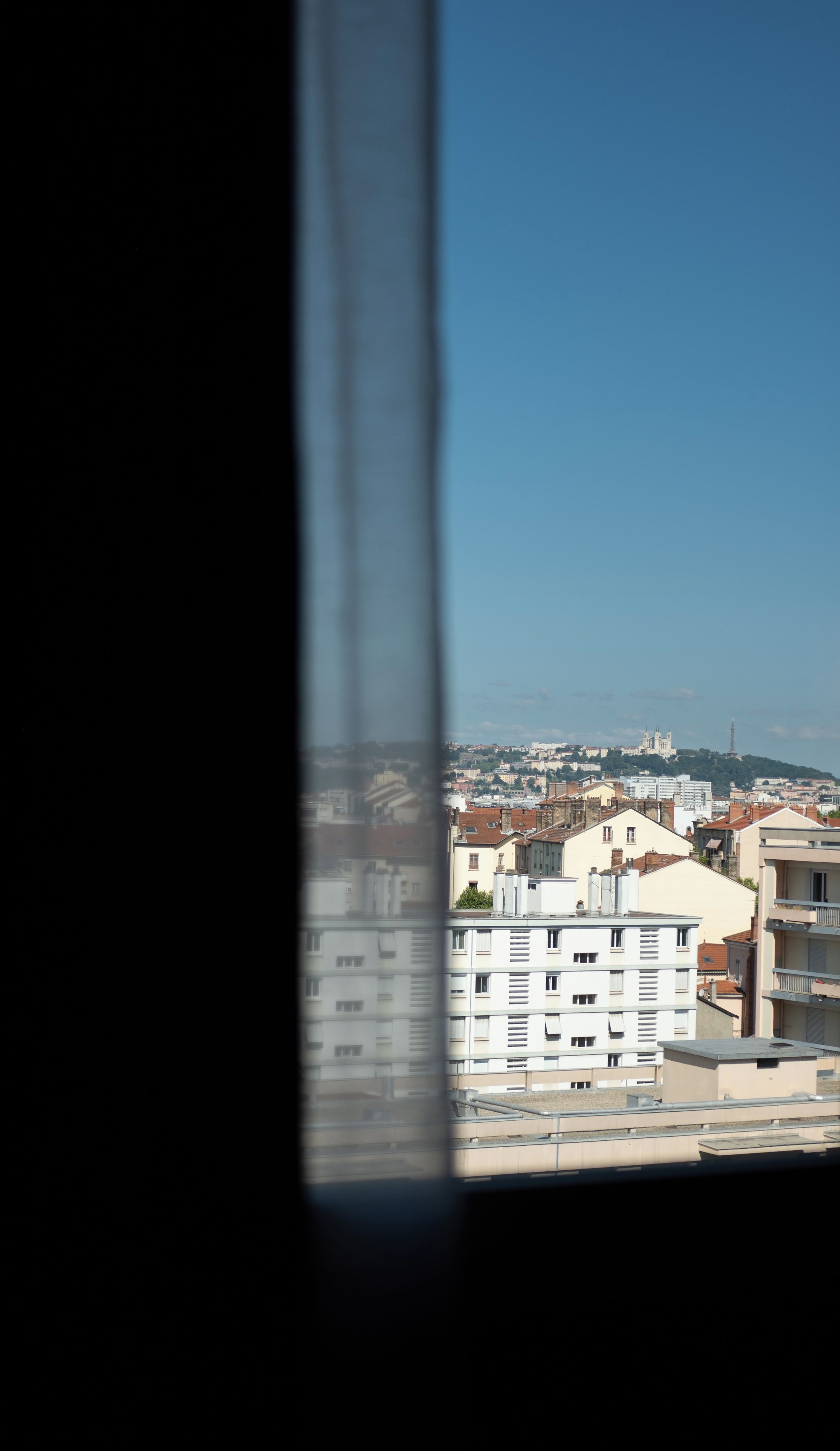 Un paisaje urbano a través de una ventana, con edificios y una colina distante.