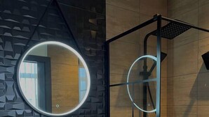 Une salle de bain moderne avec un lavabo en pierre, un miroir rond et une douche dotée d’un luminaire circulaire.