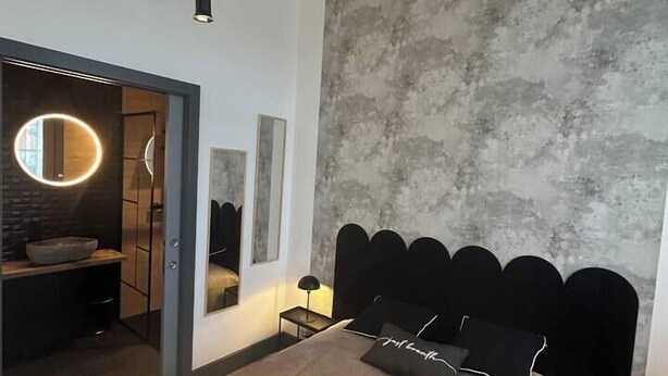 Une chambre moderne avec un grand lit, un miroir rond et un mur à texture.