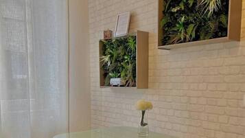 Un coin repas comprenant une table avec un plateau en verre, deux chaises, une petite plante en pot et une étagère murale agrémentée de plantes vertes.