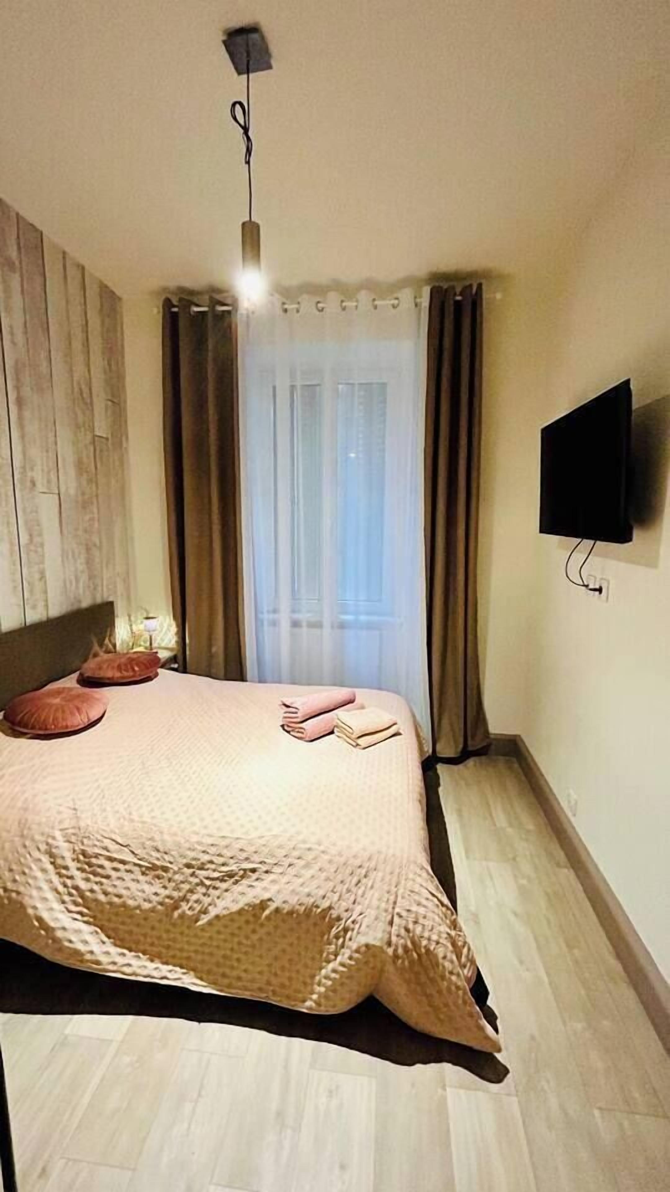 Een slaapkamer met een bed, gordijnen, een flatscreentelevisie en een houten vloer.