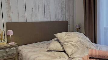 A bedroom with a wooden headboard, a bed with patterned bedding, a nightstand with a lamp, and a window with curtains.