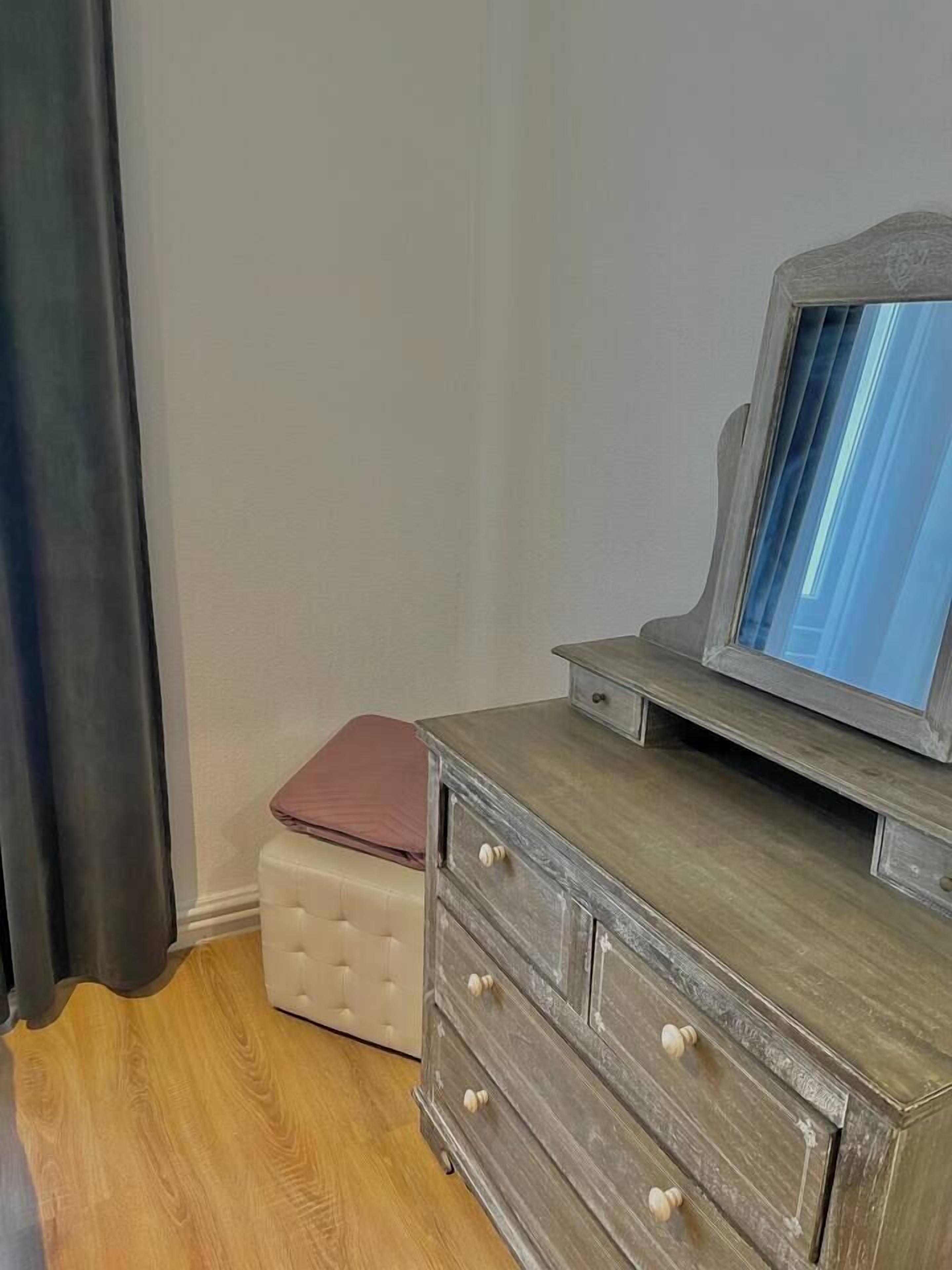 Une pièce comprenant une commode en bois, un miroir et un pouf capitonné.