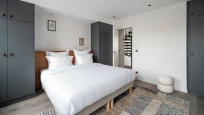 A modern bedroom with a large bed, grey wardrobes, a wooden headboard, and a staircase. - Notre-Dame Family Retreat - Authentic Paris Duplex (Paris)