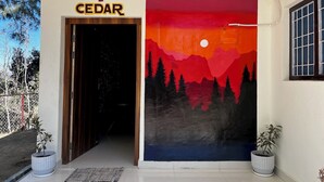 Un couloir avec une porte portant l’inscription « CEDAR » et un grand tableau représentant un coucher de soleil sur des montagnes.