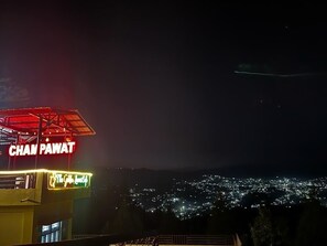 Ein Nachtblick auf eine Stadt mit einer auffälligen, rot beleuchteten Schrifttafel mit der Aufschrift 'CHAMP PAWAT' und einer entfernteren Skyline.