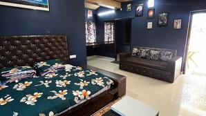 Une chambre avec un grand lit, un canapé et une petite table. Elle est éclairée par des luminaires au plafond et possède une fenêtre avec des rideaux.