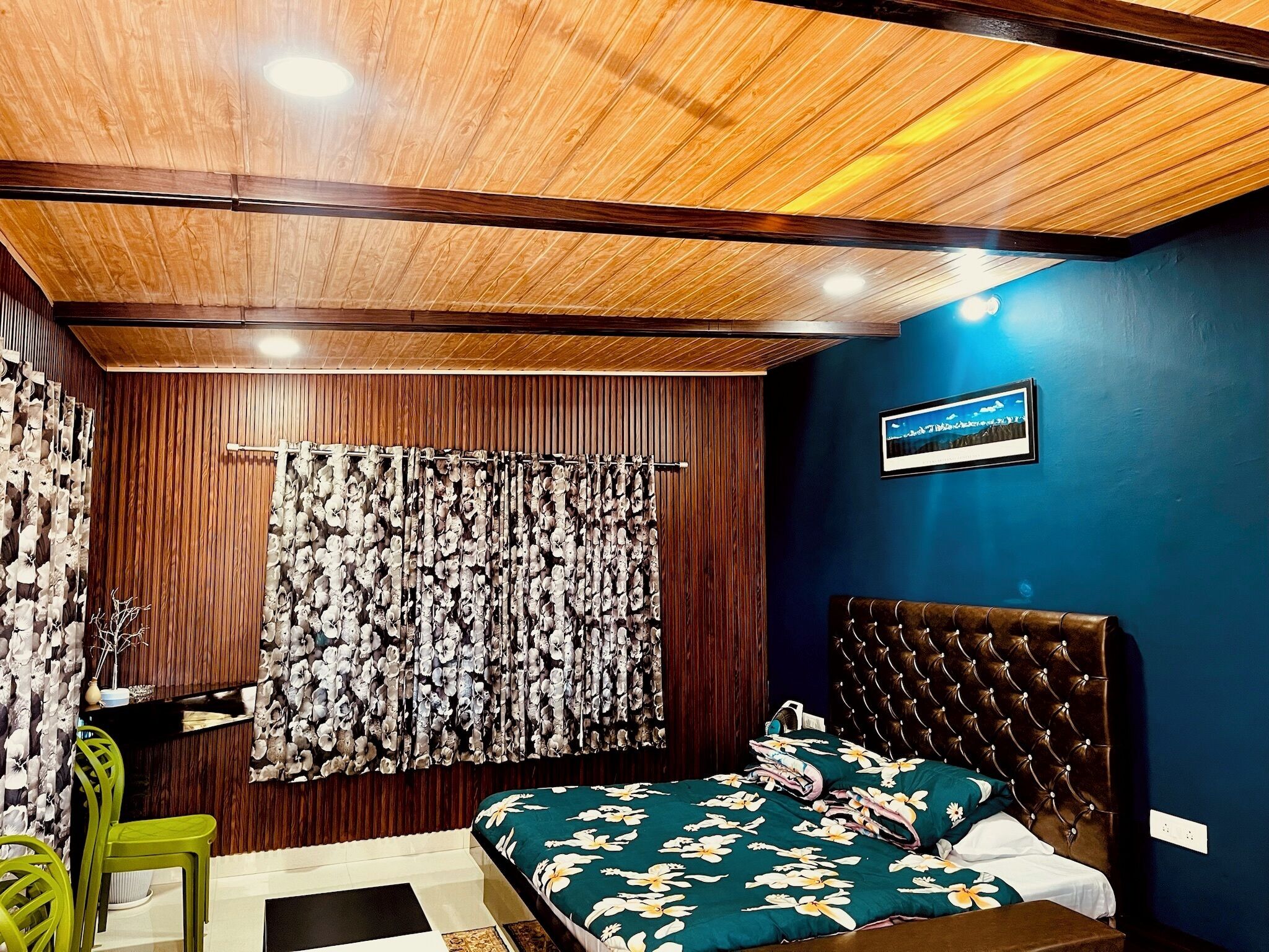 A bedroom with a wooden ceiling, a blue accent wall, a tufted headboard, floral bedding, and a curtain with a floral pattern.