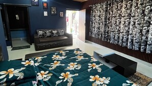Une chambre avec un plafond en bois, un lit recouvert d’une couvre-lit à motifs floraux, un canapé de couleur sombre, un mur orné d’un rideau à motifs floraux et une porte donnant sur l’extérieur.
