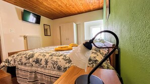 A bedroom with a wooden ceiling, a bed with floral bedding, a bedside lamp, and a window with curtains. - Leo's House (Carbonare)