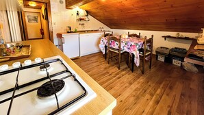 A compact kitchen with a gas stove, wooden ceiling, and a dining table set for four. - Leo's House (Carbonare)
