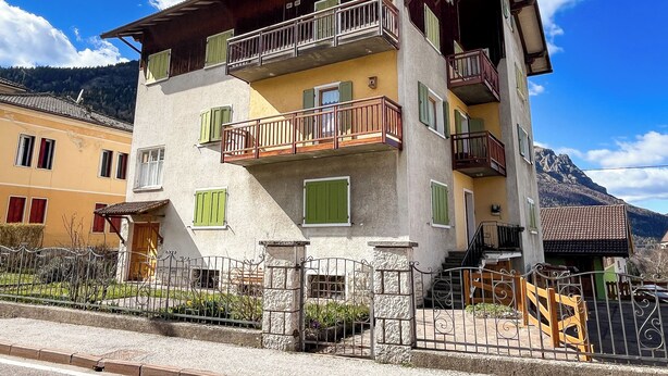 A multi-story building with balconies, a stone facade, and a mountain backdrop. - Leo's House (Carbonare)