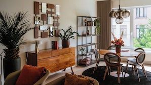 Una sala de estar moderna con un aparador de madera, una mesa de comedor redonda con sillas, una estantería y un ventanal con vistas a zonas verdes.