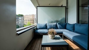 Un balcón con un sofá azul, una mesa con una planta y vistas a edificios.
