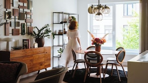 Una sala de estar moderna con un mueble de madera, una mesa redonda con sillas, una planta en maceta y un ventanal con vistas a la vegetación.