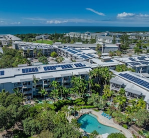 Un resort con diversi edifici, pannelli solari sui tetti, una piscina e vista sull'oceano.