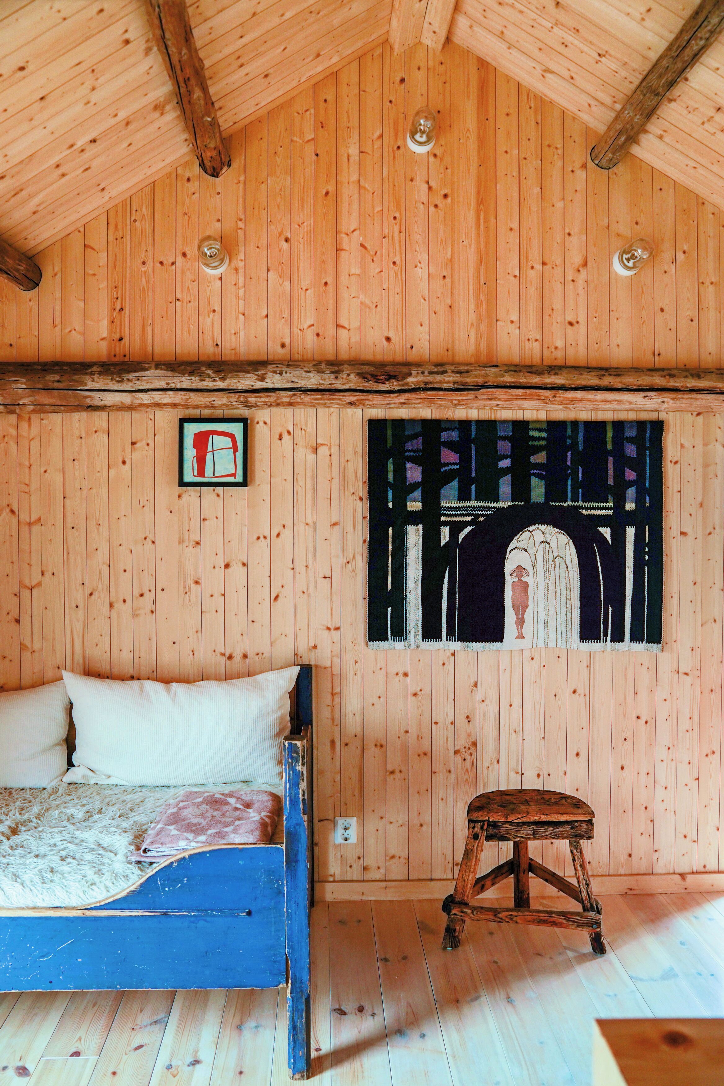A wooden room with a bed, a stool, and a wall painting.