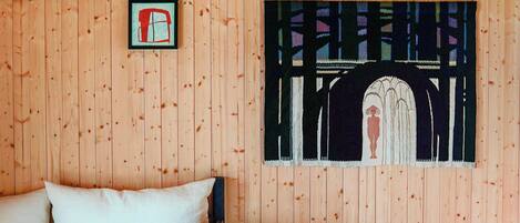 A wooden room with a bed, a stool, and a wall painting.
