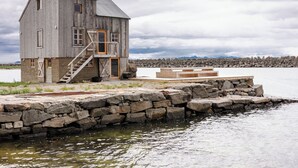 A wooden house with a staircase, a dock, and a rocky shoreline. - Villa Lofoten (Bøstad)