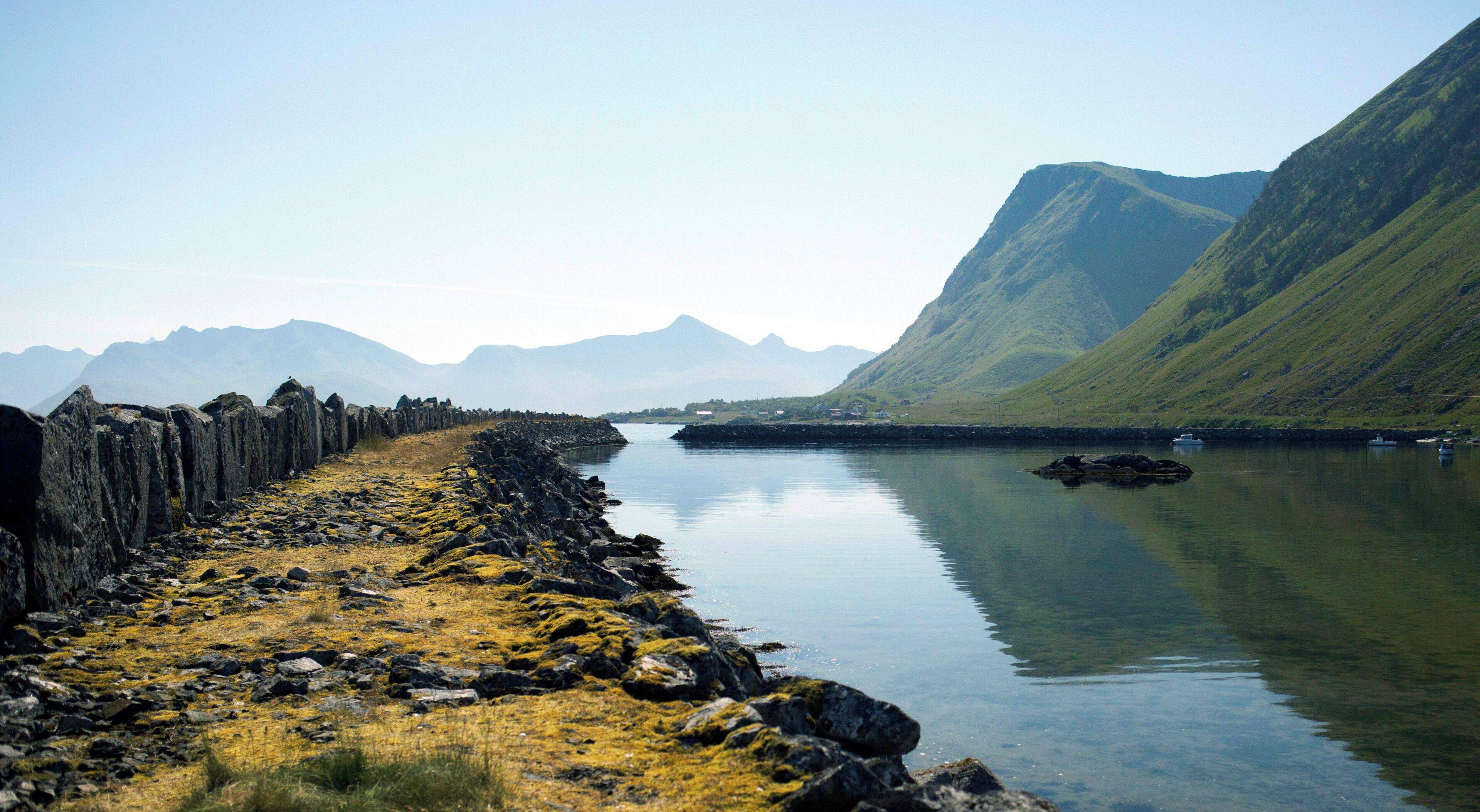 A calm lake with a rocky shoreline, a boat, and mountains in the background.