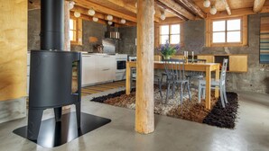 A rustic kitchen with a wood-burning stove, a dining table with chairs, and a large window. - Villa Lofoten (Bøstad)