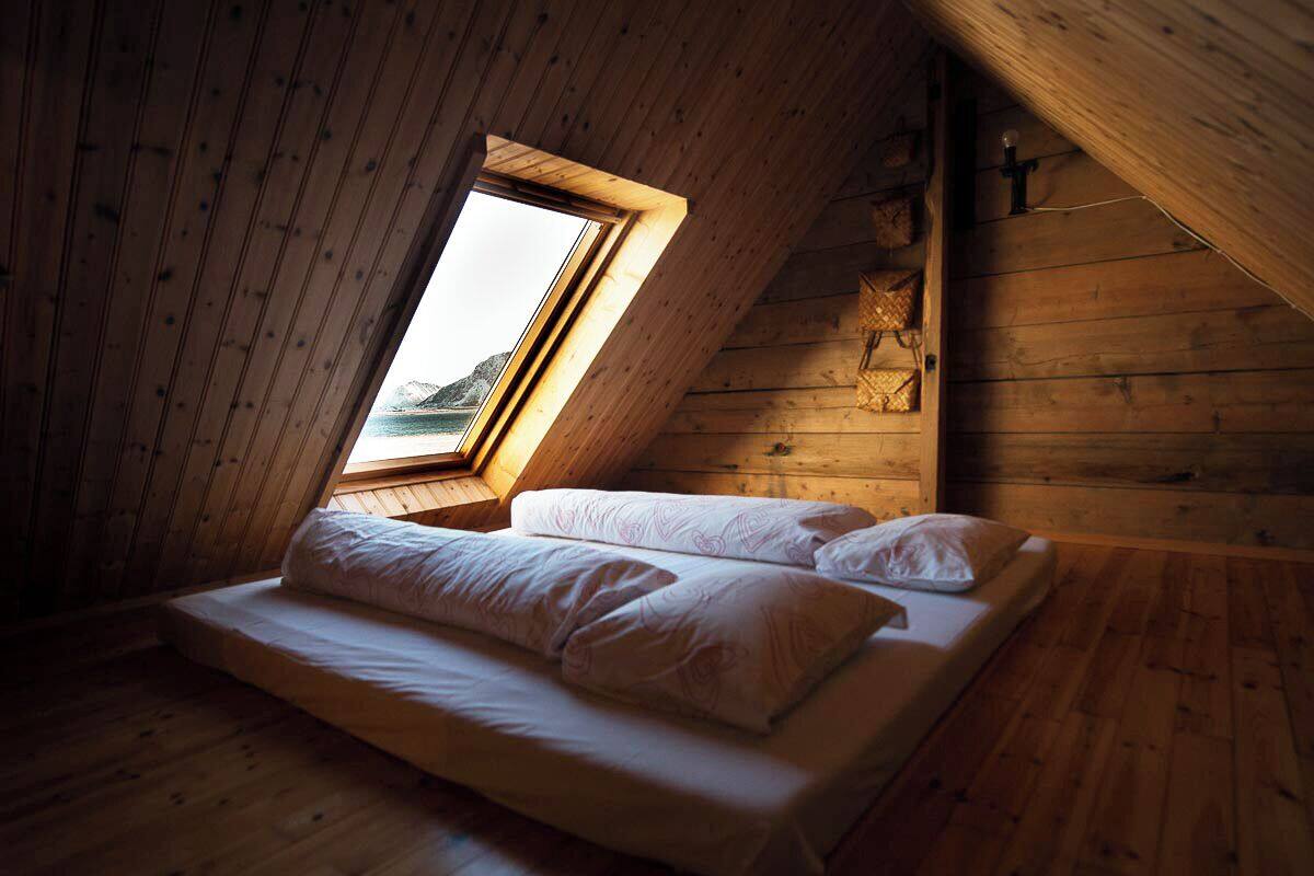 Un dormitorio de cabaña de madera con techo inclinado, una cama individual y una ventana con vistas a un paisaje montañoso.