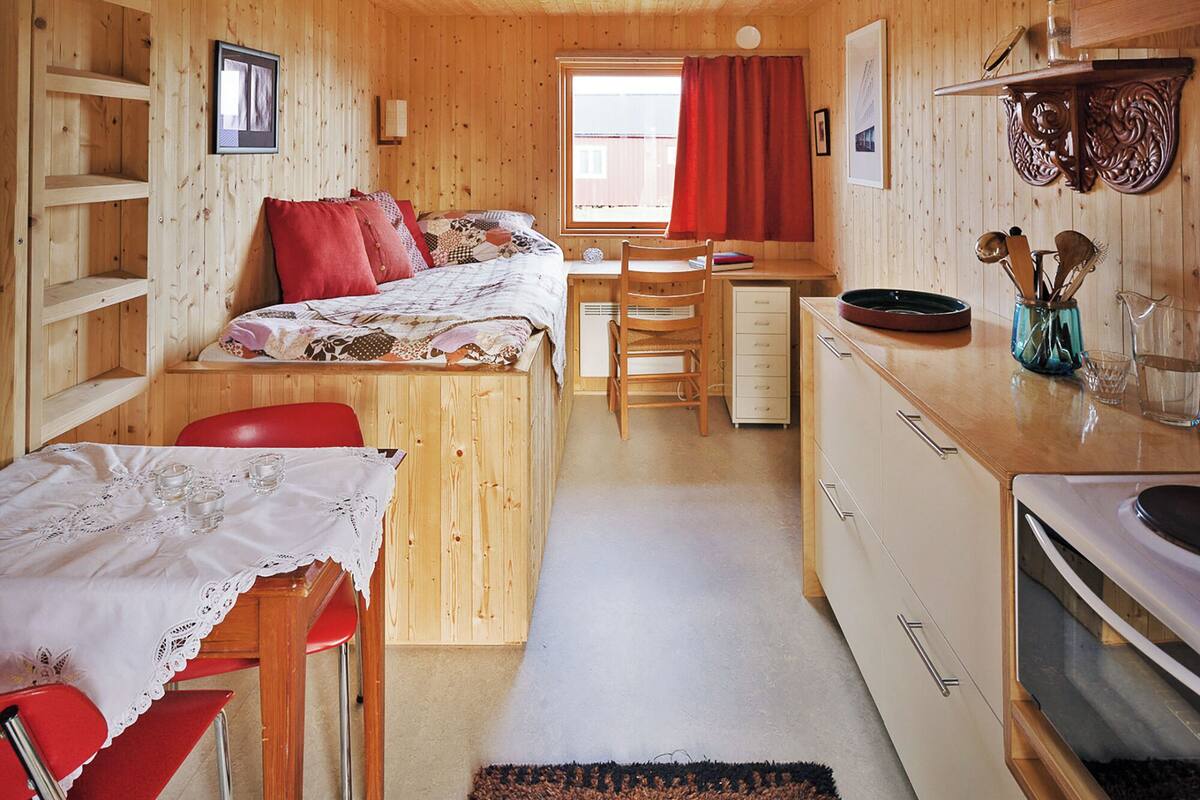 Una cabaña acogedora con literas, una mesa de comedor, una zona de cocina y un ventanal con cortinas.