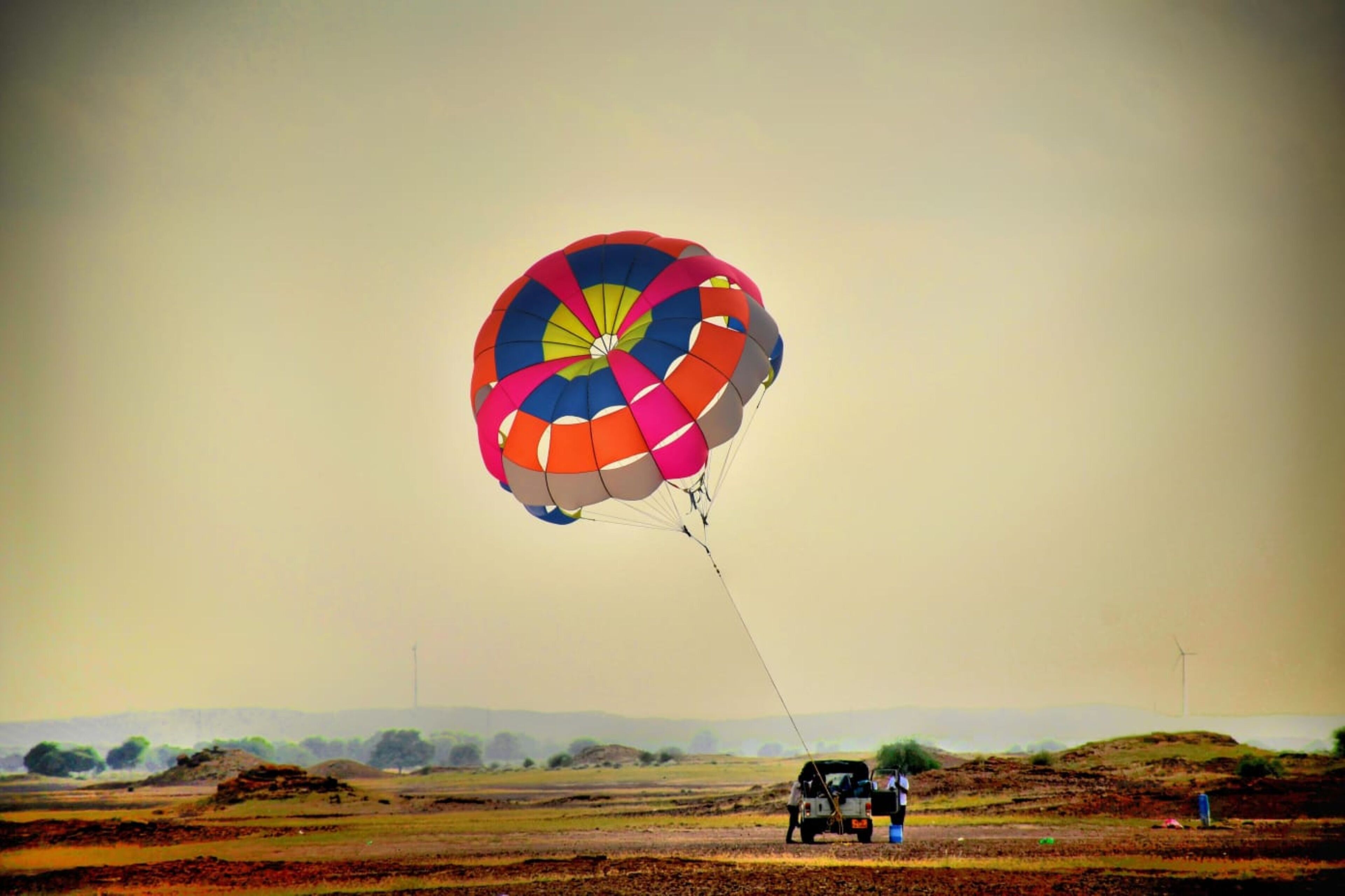 A vehicle with a parachute on a flat landscape.