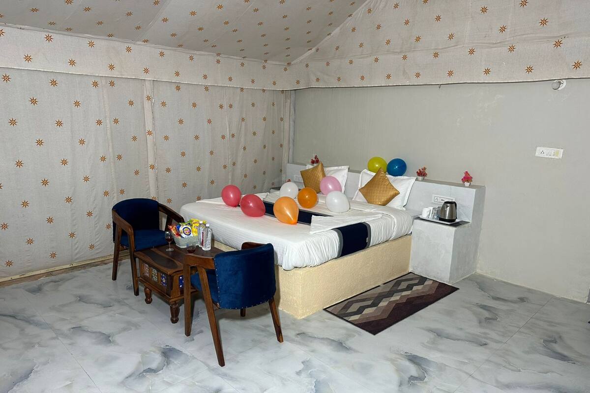Una habitación de hotel con cama, una mesita pequeña con sillas y una mesita de noche con hervidor.