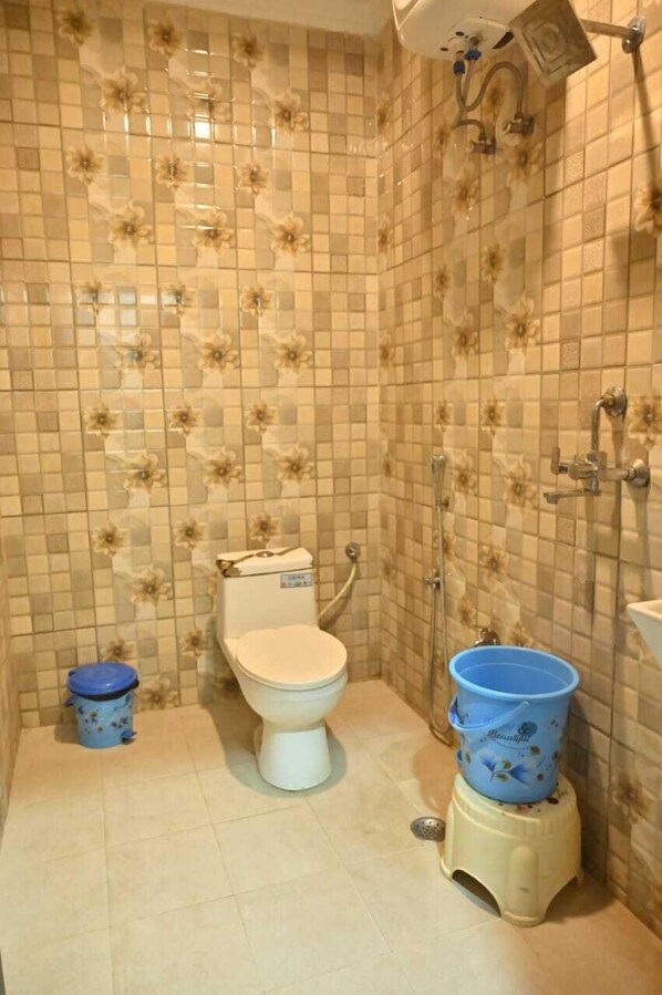 A bathroom with a toilet, a blue trash bin, a blue bucket, and a shower area. - Banarasi Kothi (Varanasi)