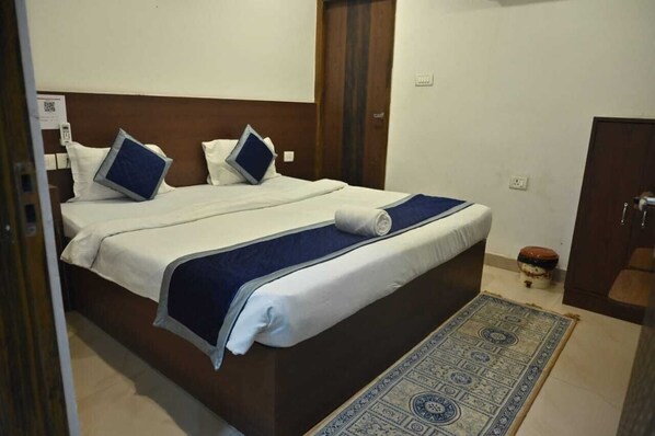 A neatly made bed with a blue and white bedspread, a matching blue pillow, and a small round table with a red lid. - Banarasi Kothi (Varanasi)