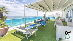 Ein überdachter Außenbereich mit Pool, Liegestühlen und Tischen, mit Blick auf das Meer.