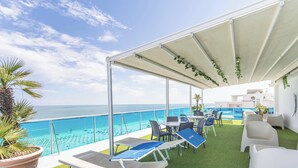 Un espacio de estar al aire libre techado con vista al océano, equipado con sillones y mesas.