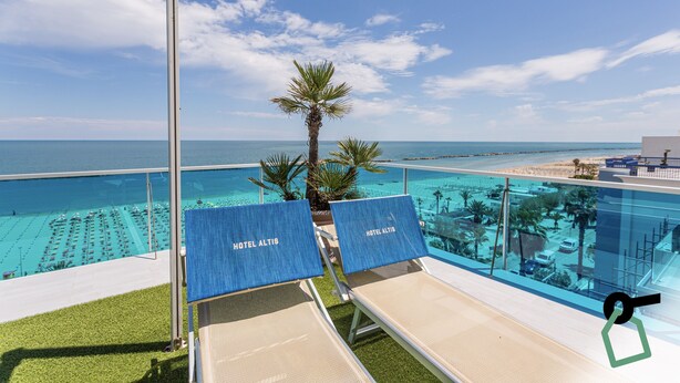 Ein Poolbereich mit Liegestühlen, beschriftet mit 'HOTEL ALTIS', mit freiem Blick auf den Ozean und einer Palme.