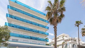 Un hotel moderno con varios balcones, una entrada principal y palmeras.