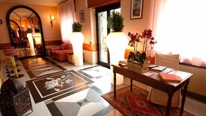 A hotel lobby with a checkered floor, a sofa, a table with a vase of flowers, and a mirror. - hotel san gerolamo (Vercurago)