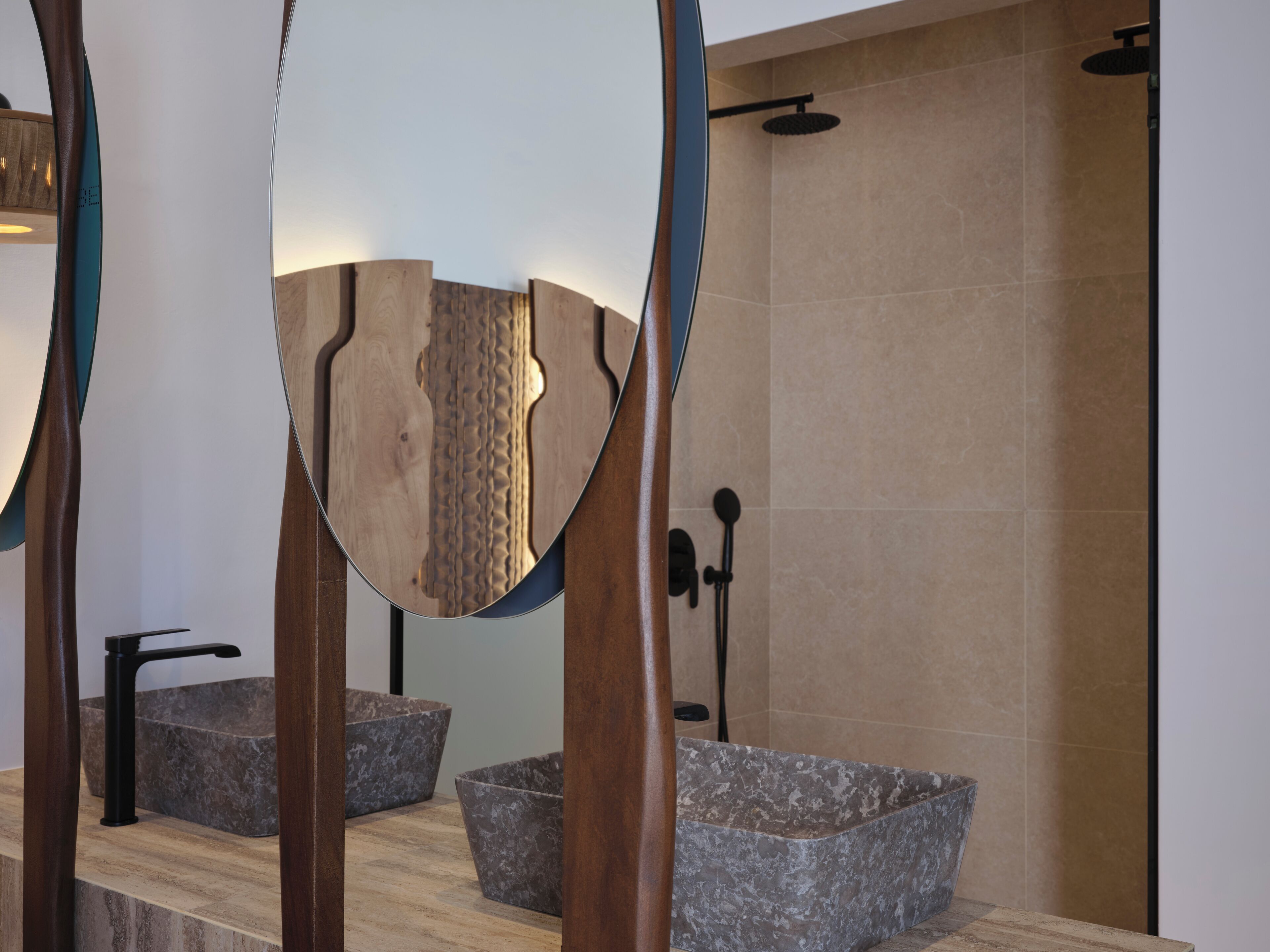 A modern bathroom with a large mirror, two granite sinks, and a shower area.