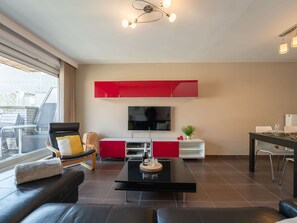 Uma sala de estar moderna com um sofá preto, uma mesa de centro, uma televisão e armários vermelhos.