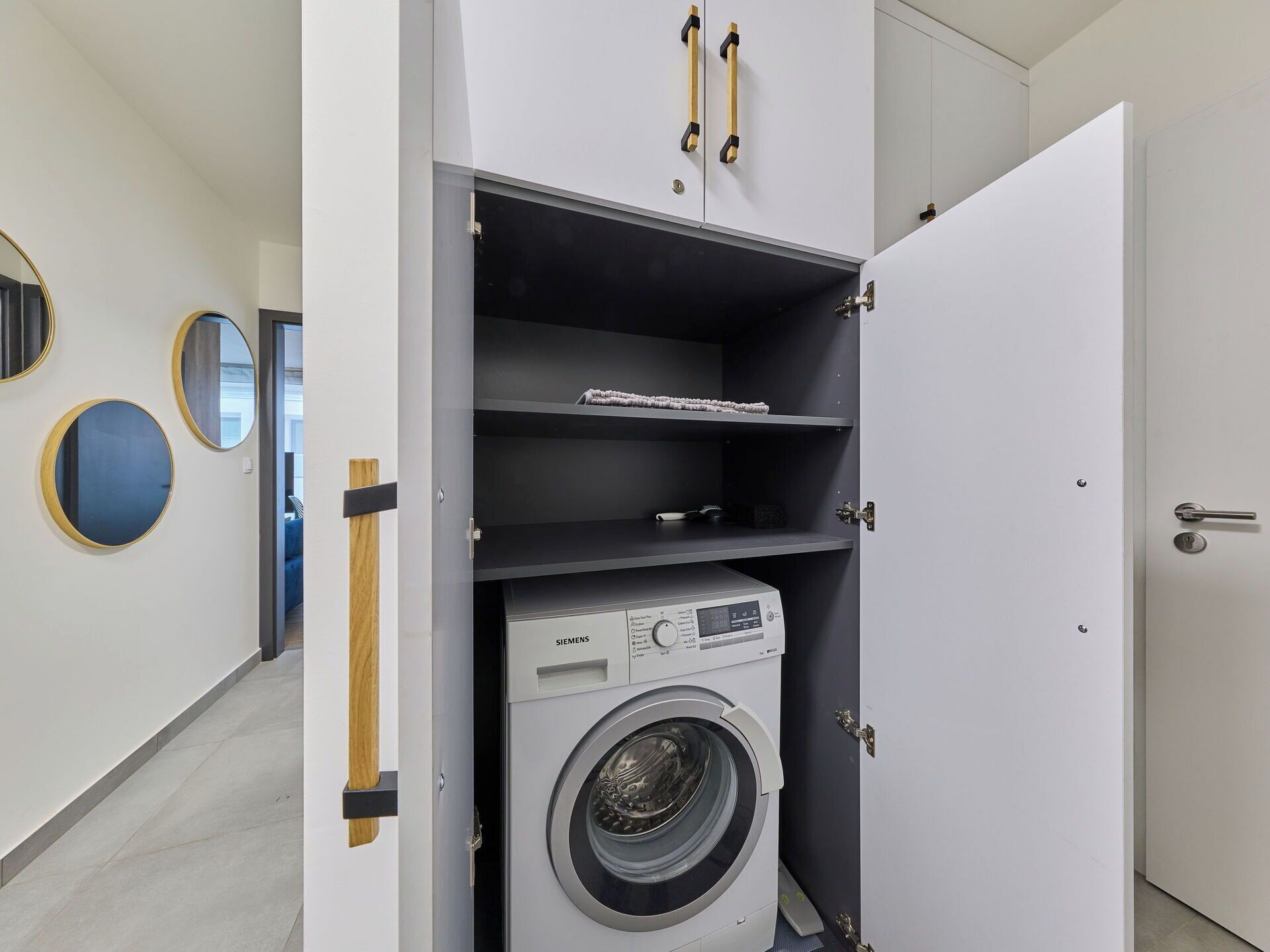 A compact laundry room with a front-loading washing machine, a small shelf with a towel, and a door with a handle.