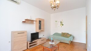 A modern living room with a wooden cabinet, a flat-screen TV, a glass coffee table, and a green sofa.