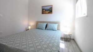 Un dormitorio con una cama, un cuadro en la pared y una pequeña mesa con una vela.