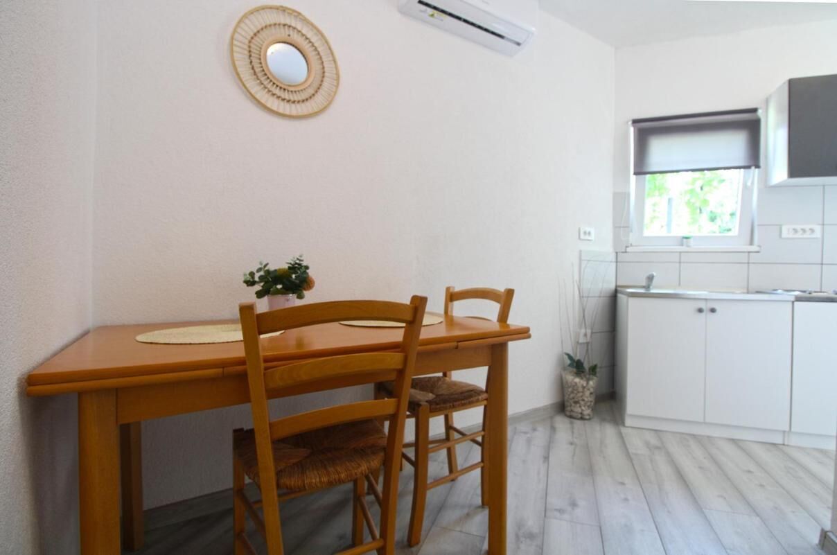 A small kitchen with a wooden table and chairs, a potted plant, and white cabinets.