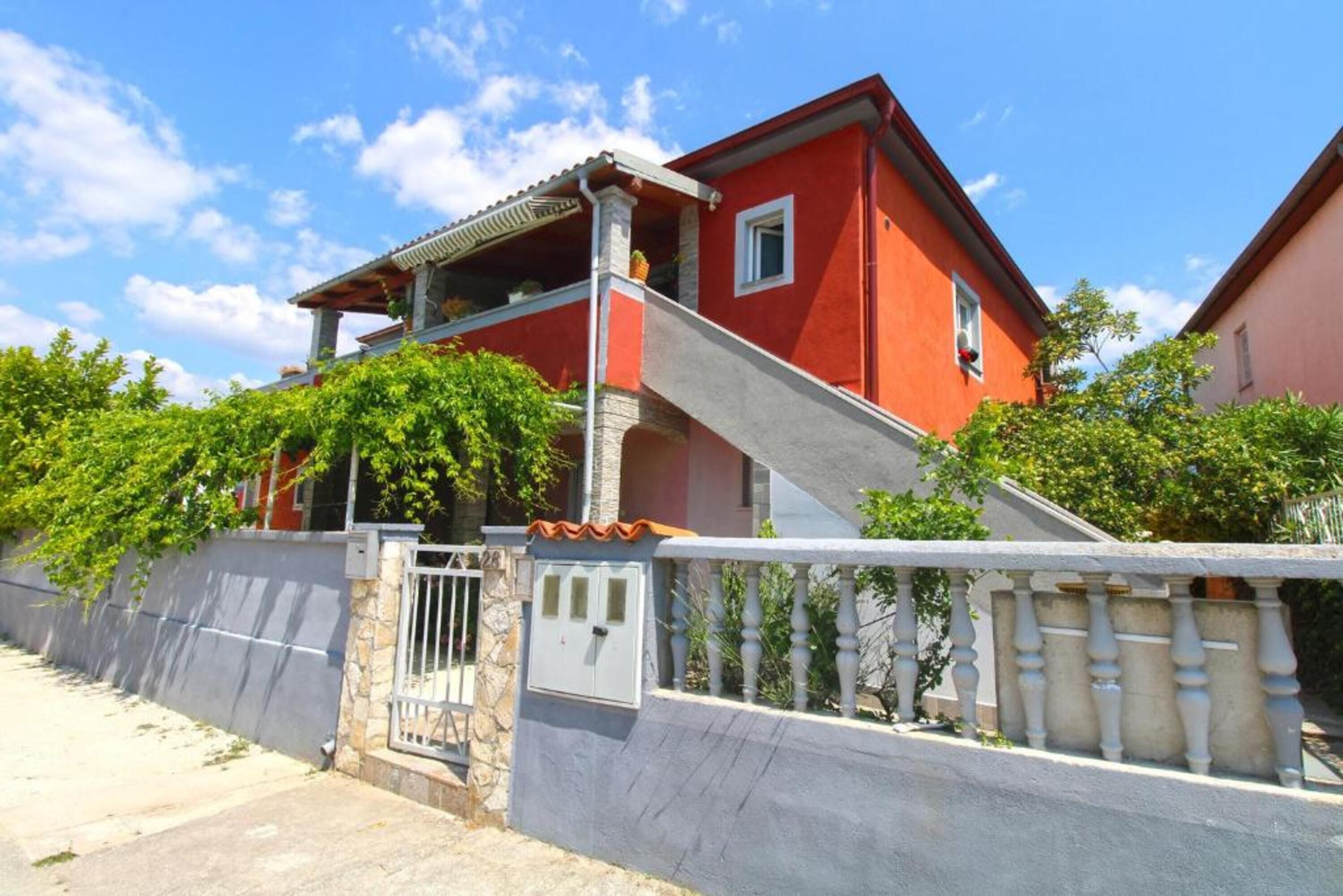 Une maison à deux étages avec une façade rouge, un mur en pierre et une entrée fermée par un portail.