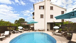 A swimming pool with lounge chairs and umbrellas, surrounded by a building with balconies. - Charming accommodation with shared pool Beahost (Peroj)