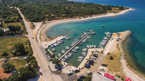 An aerial view of a marina with boats docked, a road adjacent to the water, and a beach area. - Charming accommodation with shared pool Beahost (Peroj)