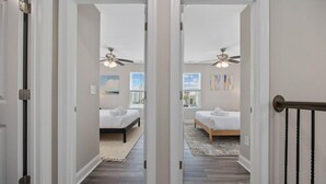 A hallway leading to two bedrooms with ceiling fans, a rug, and artwork on the walls. - Capers Blade-Across Beach-Garage (Myrtle Beach)
