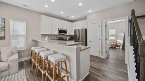 A modern kitchen with white cabinets, stainless steel appliances, and a central island with bar stools. - Capers Blade-Across Beach-Garage (Myrtle Beach)